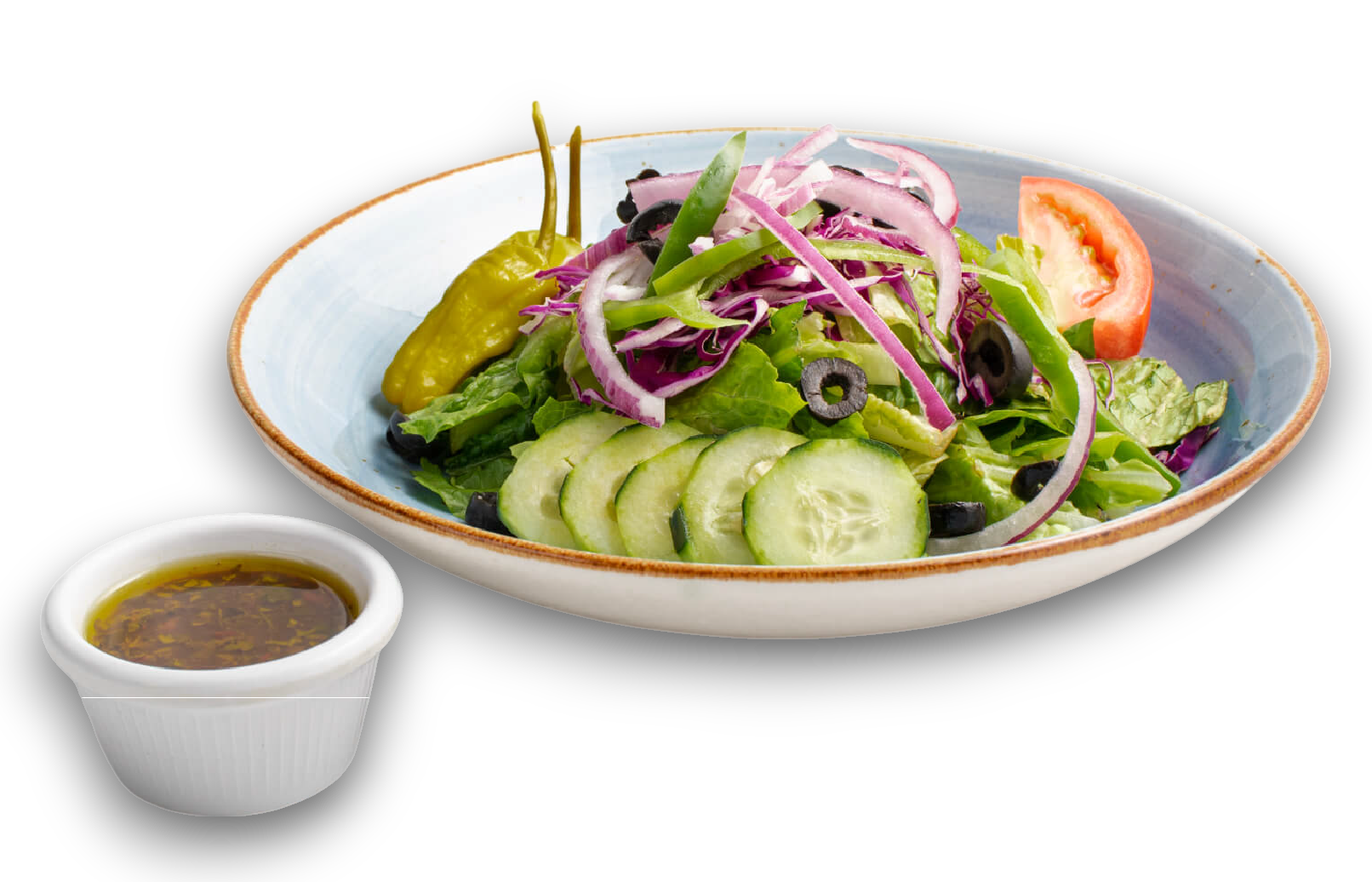 A garden salad in a shallow bowl with cucumber, red onion, and a pepperoncini, served with a side of dressing.