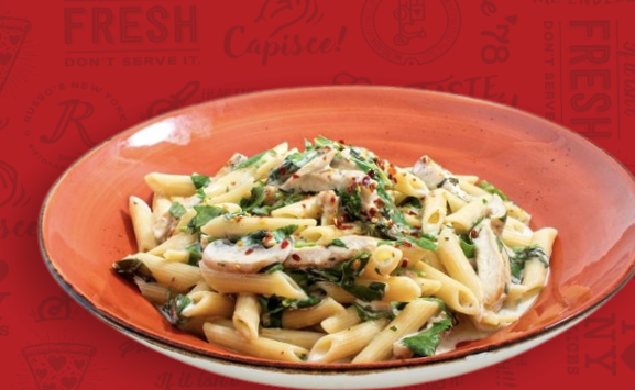 Plate of penne pasta with creamy sauce and herbs on a red restaurant-style background