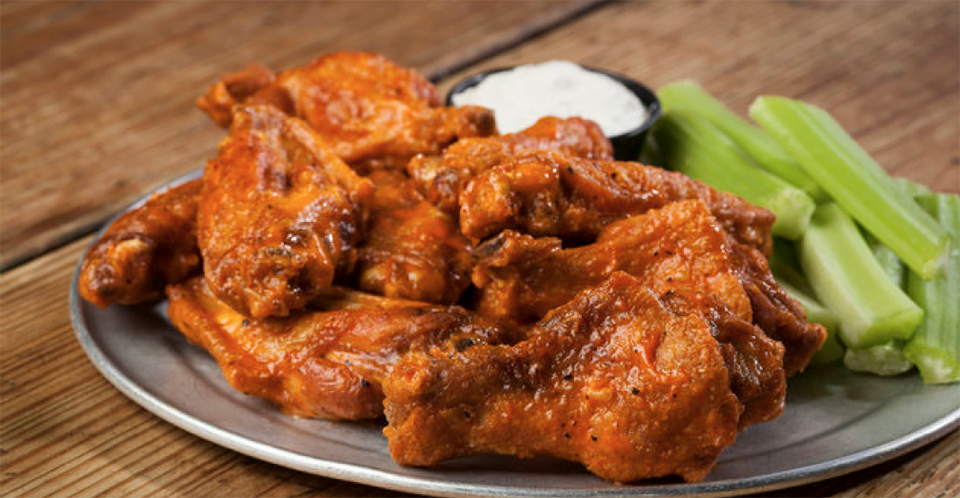 Buffalo wings with dipping sauce and celery sticks on a metal plate.