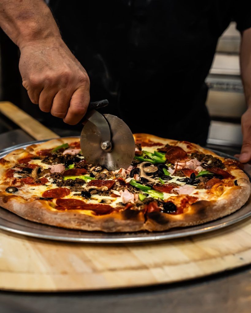 Pizza being sliced with a pizza cutter on a wooden peel.