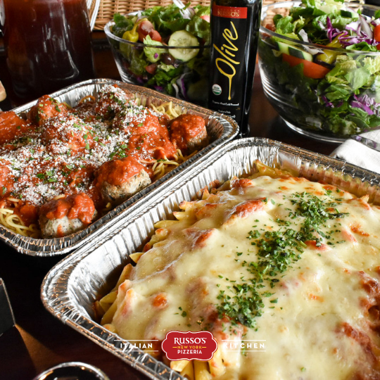 Italian meal with baked pasta, saucy entree, and salads on a table