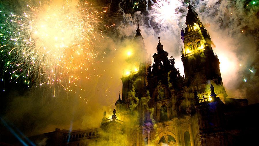 Una catedral está iluminada con fuegos artificiales en el fondo.