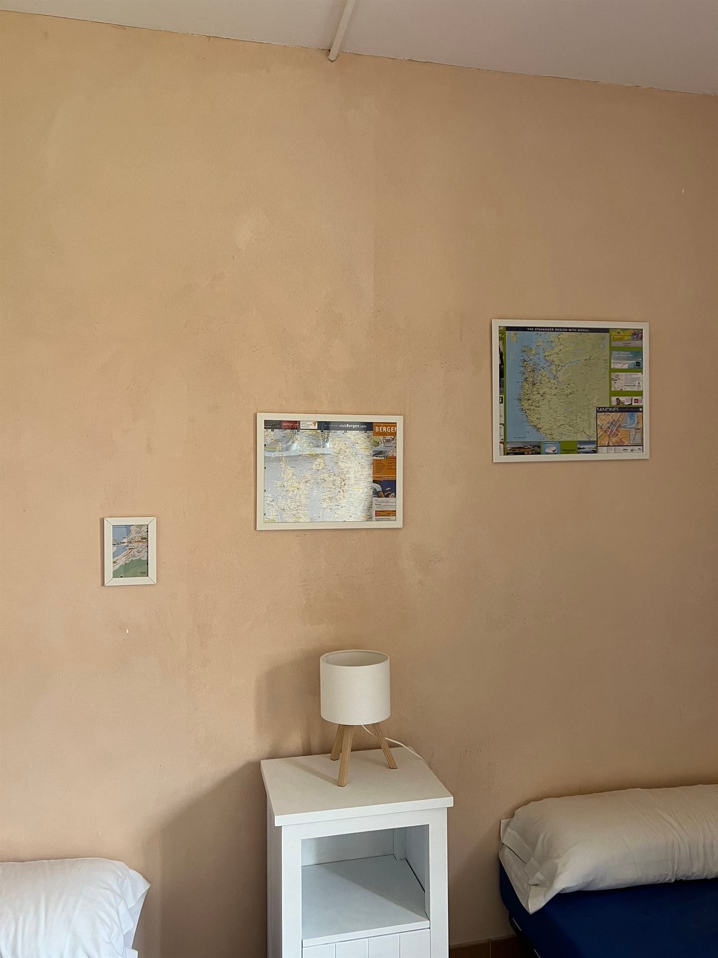 Un dormitorio con una cama, mesita de noche, lámpara y mapas en la pared.