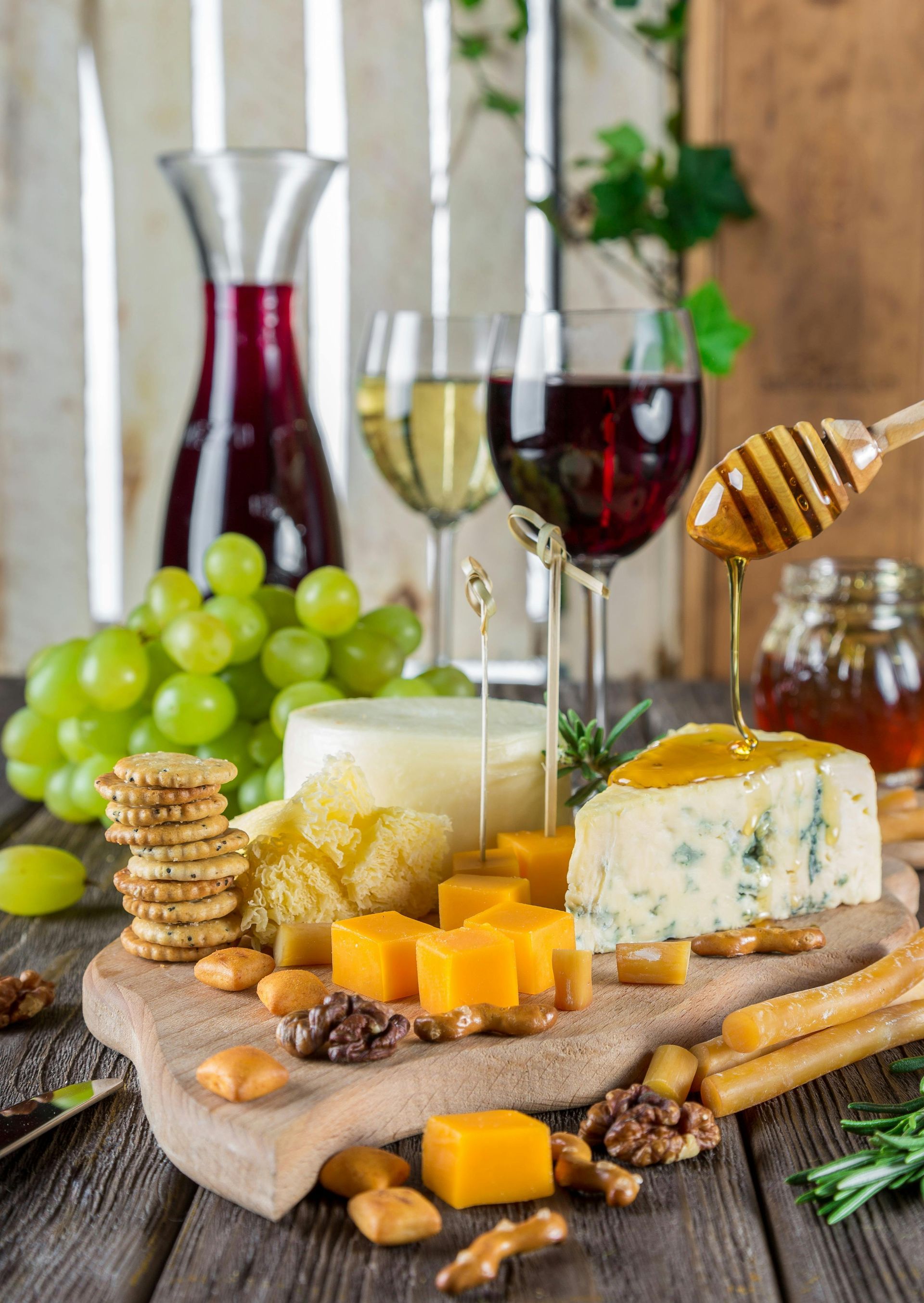 Una tabla de cortar de madera cubierta con queso, galletas, nueces, uvas y copas de vino.