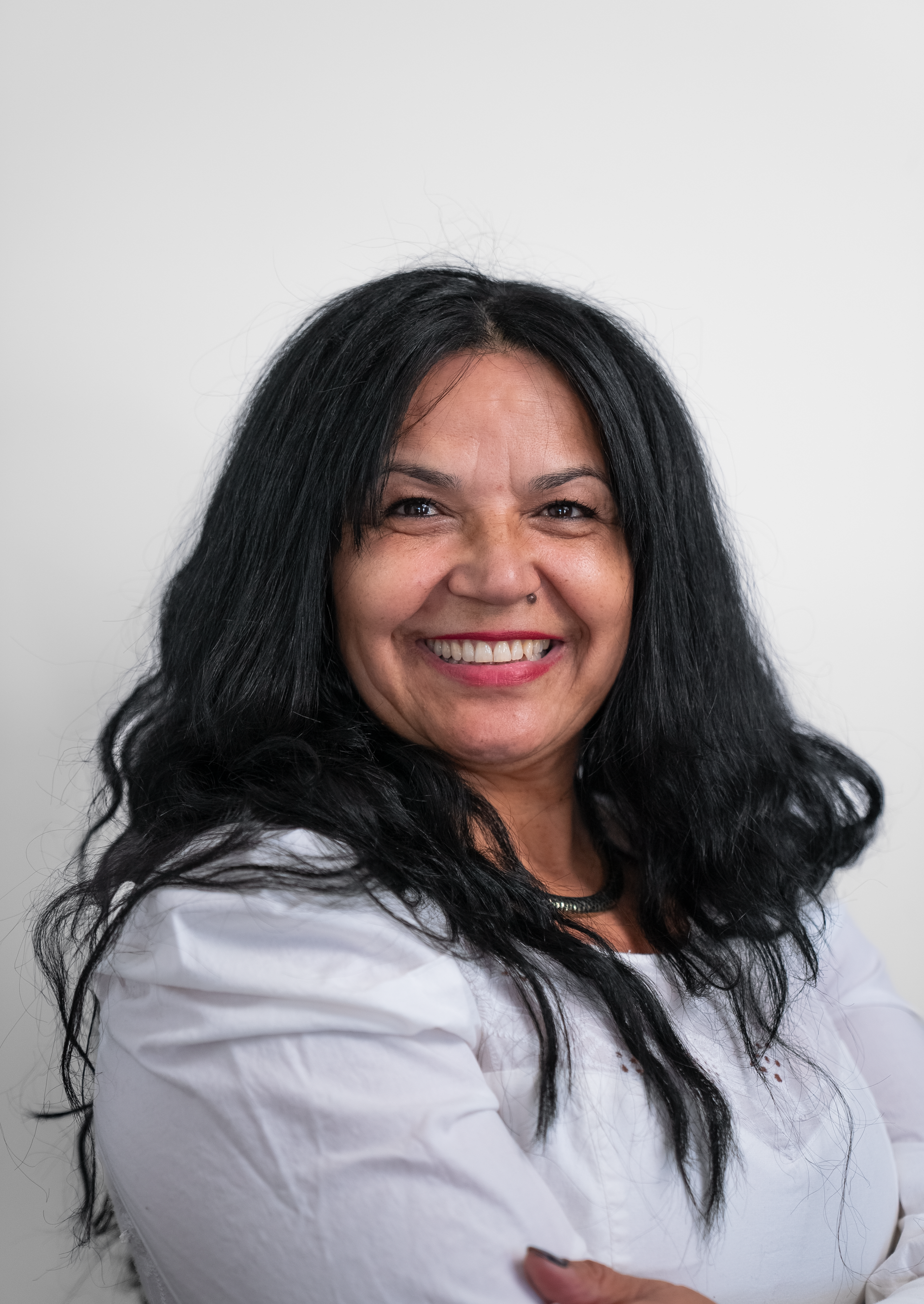 A woman with long black hair is smiling and wearing a white shirt.