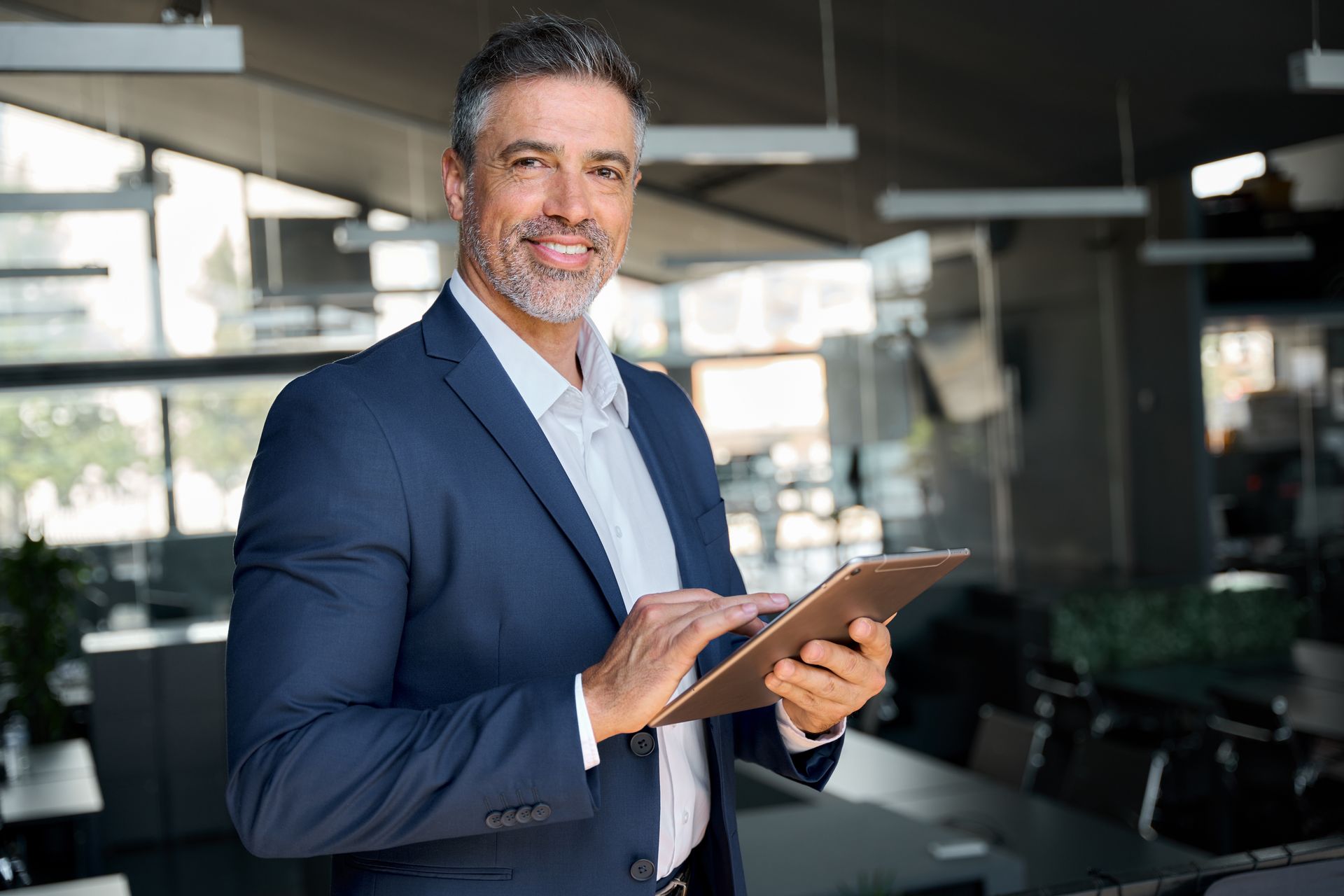 A man in a suit is holding a tablet in an office.