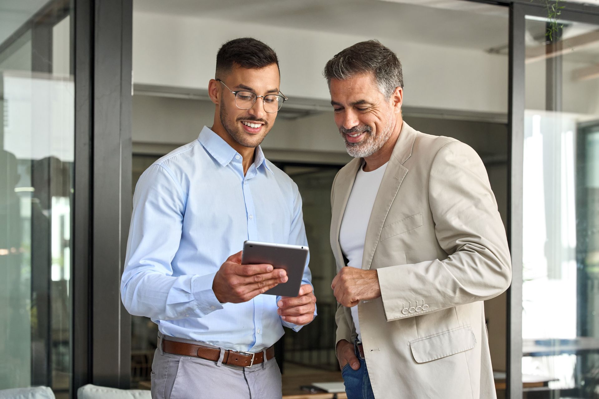 Two men are looking at a tablet together in an office.