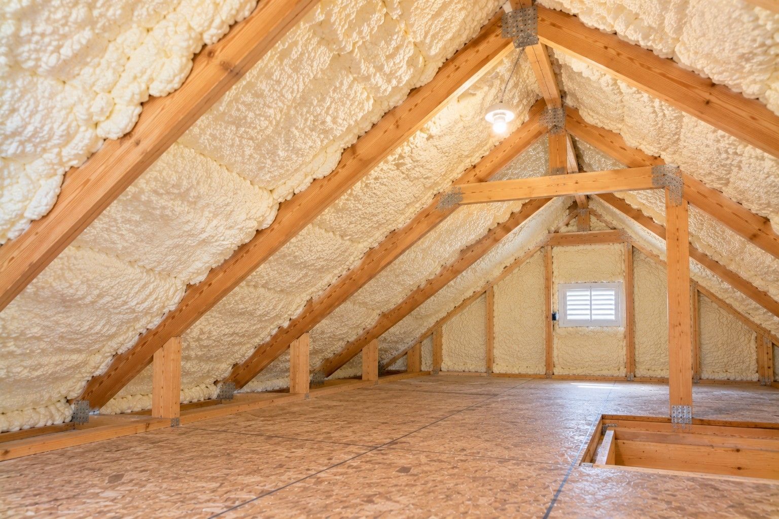 Completed attic spray foam insulation covering sloped roof decking and exposed wooden rafters, featuring thick foam coverage, structural beams, a ventilation opening, and plywood flooring in a residential home in Taunton, Massachusetts.