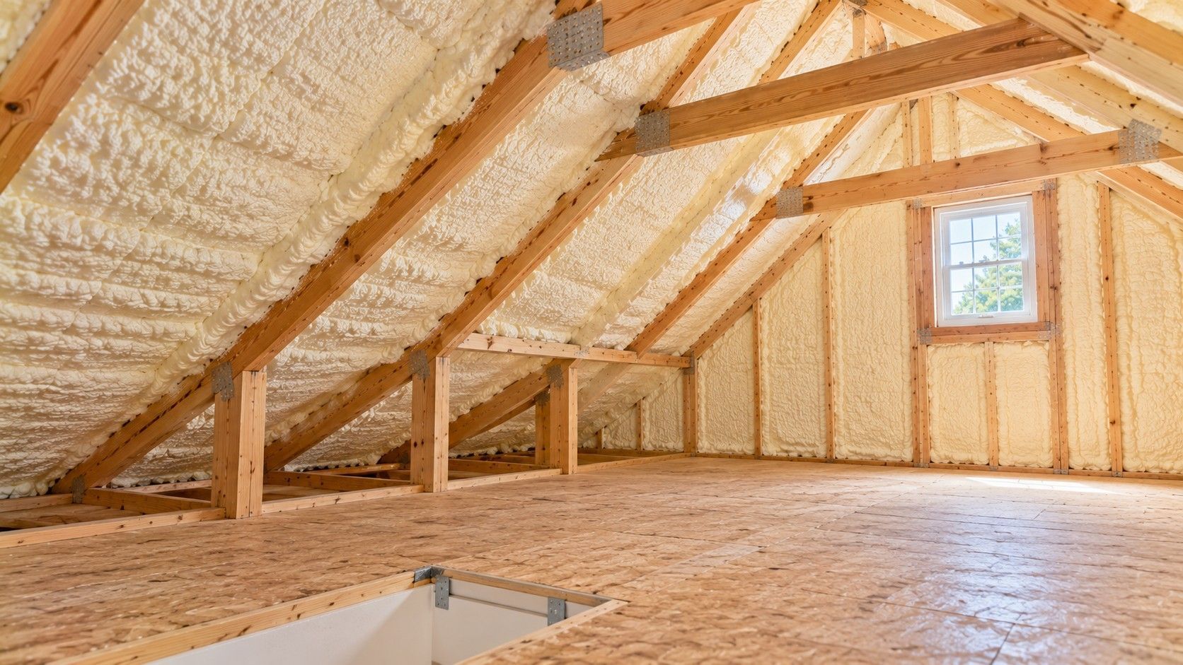 Completed spray foam insulation between engineered roof rafters and gable wall framing inside a modern residential attic in Taunton, Massachusetts.