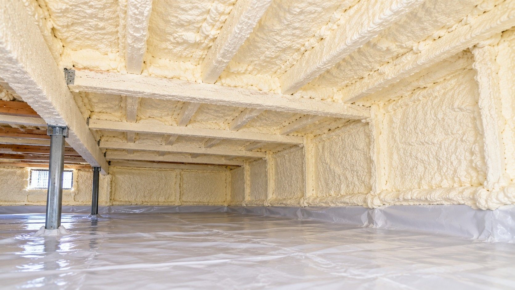 Completed crawl space spray foam insulation covering foundation walls, ceiling cavities, and wooden floor joists, featuring sealed surfaces, support posts, and a clean vapor barrier in a residential crawl space in Fall River, Massachusetts.