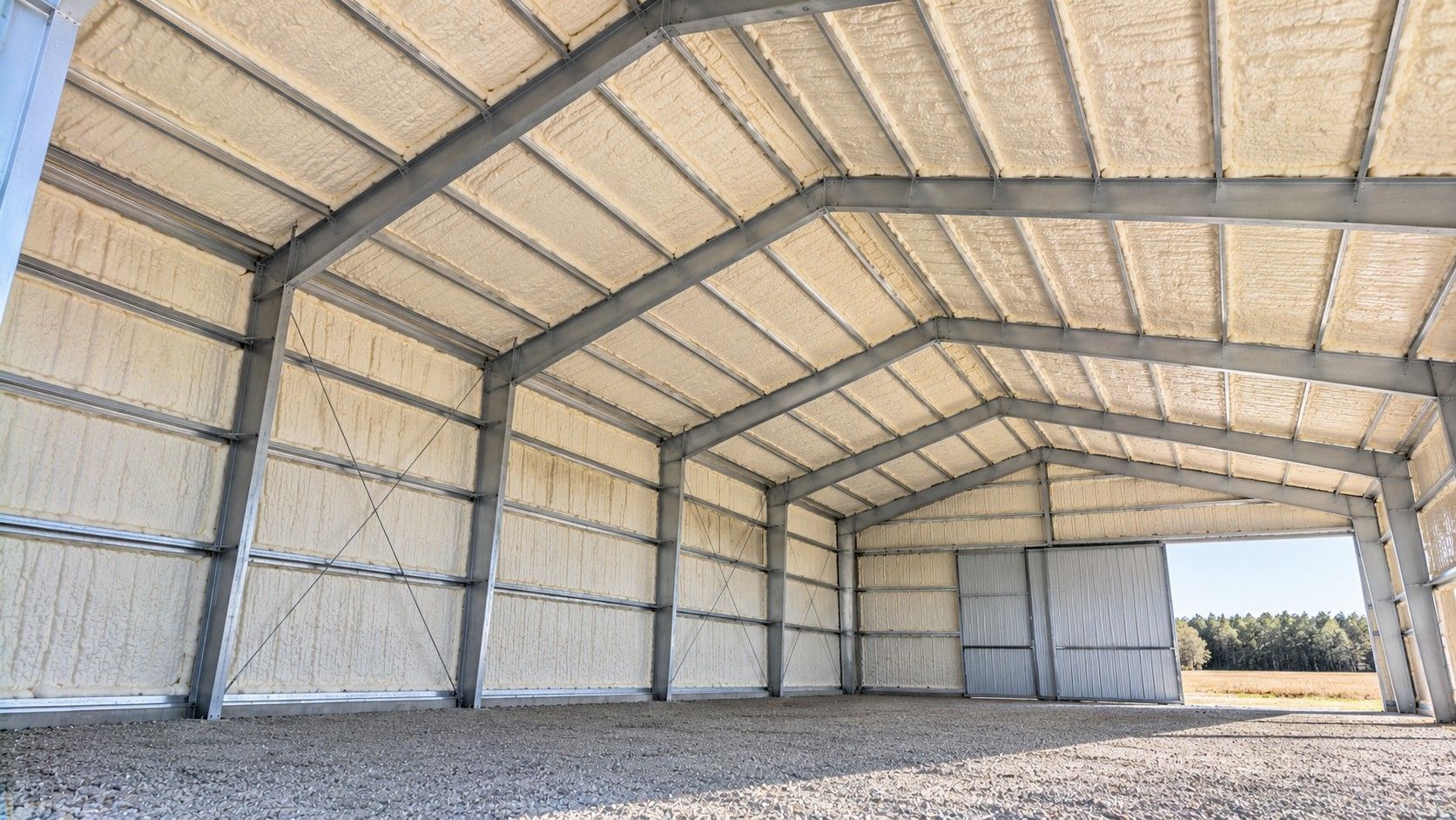 Finished spray foam insulation covering the metal roof and interior walls of an agricultural equipment storage building.