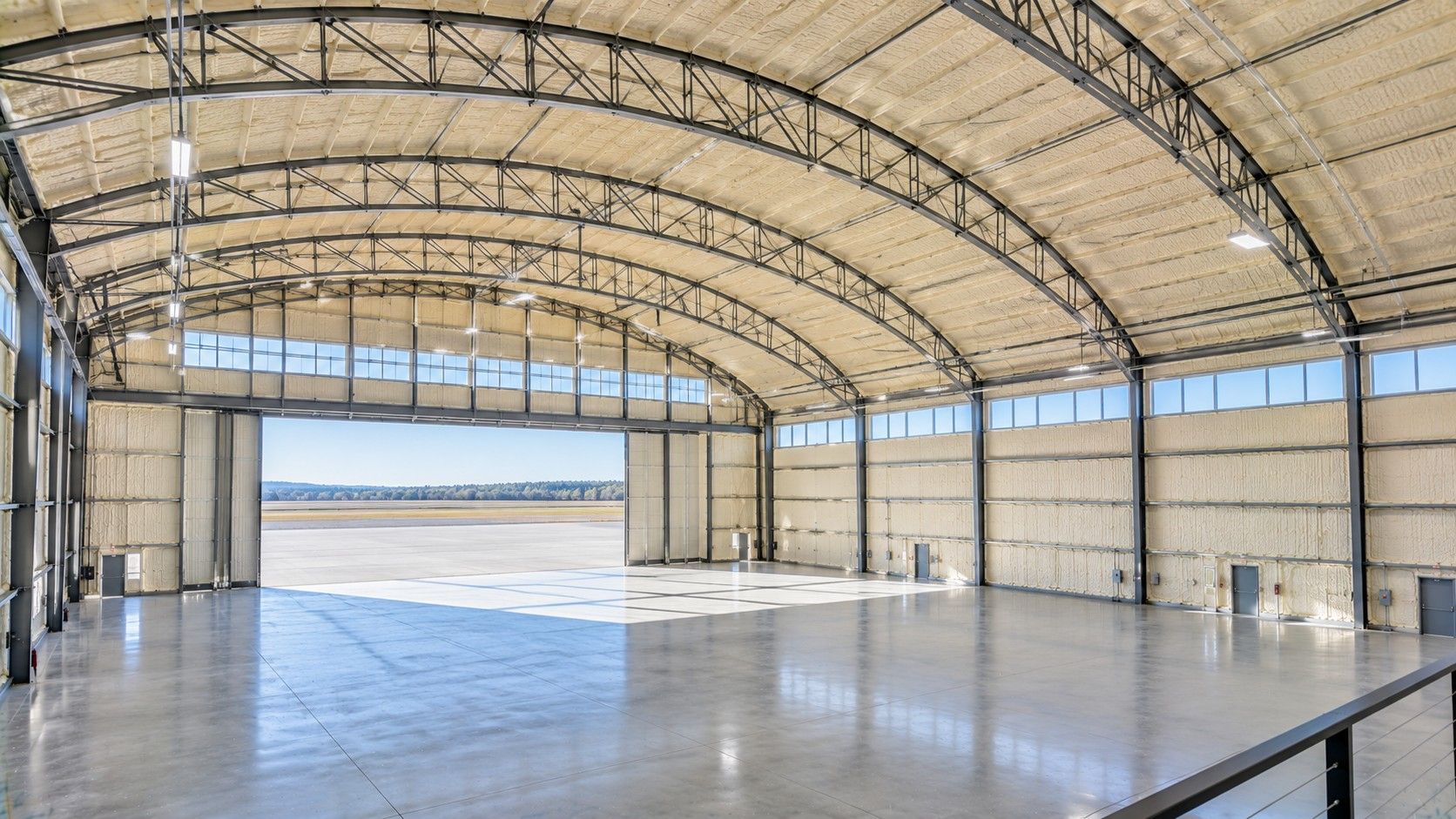 Completed spray foam insulation covering the curved metal roof and interior walls of a spacious aircraft hangar.