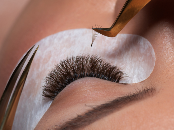 Close-up of eyelash extension application with tweezers and eye pad beneath the eyebrow
