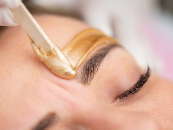 Eyebrow being shaped with wax on a closed eye in a close-up beauty treatment
