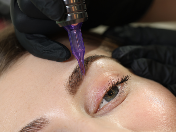 Microblading tool shaping a dark eyebrow on a close-up of a person's face
