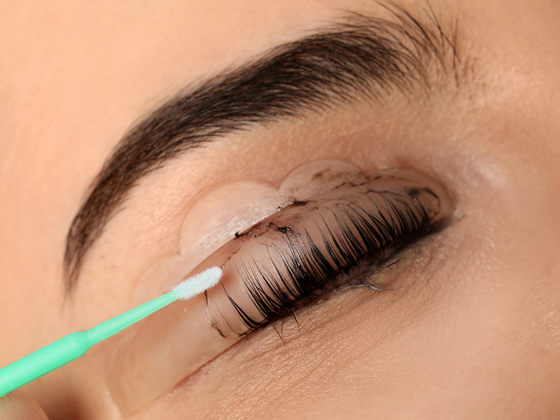 Close-up of an eyelid being applied with eye cream using a green applicator stick