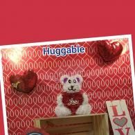 Red Valentine-themed display with a teddy bear, heart decorations, and the word “Huggable”