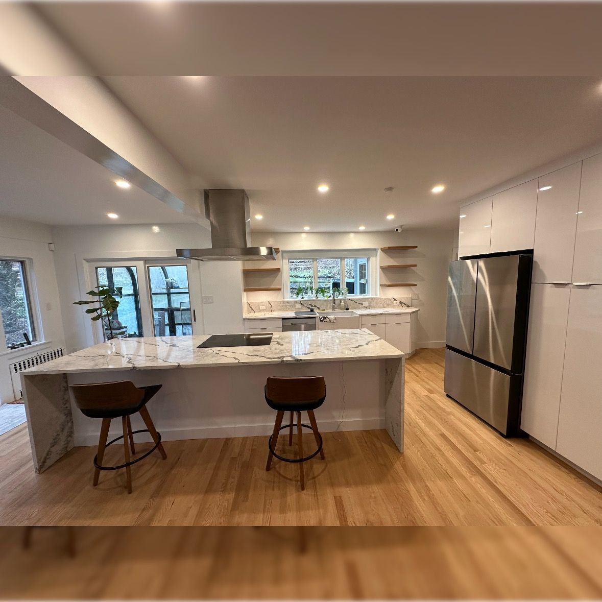 Modern kitchen with white cabinets, marble island, stainless fridge, and two stools on hardwood floors