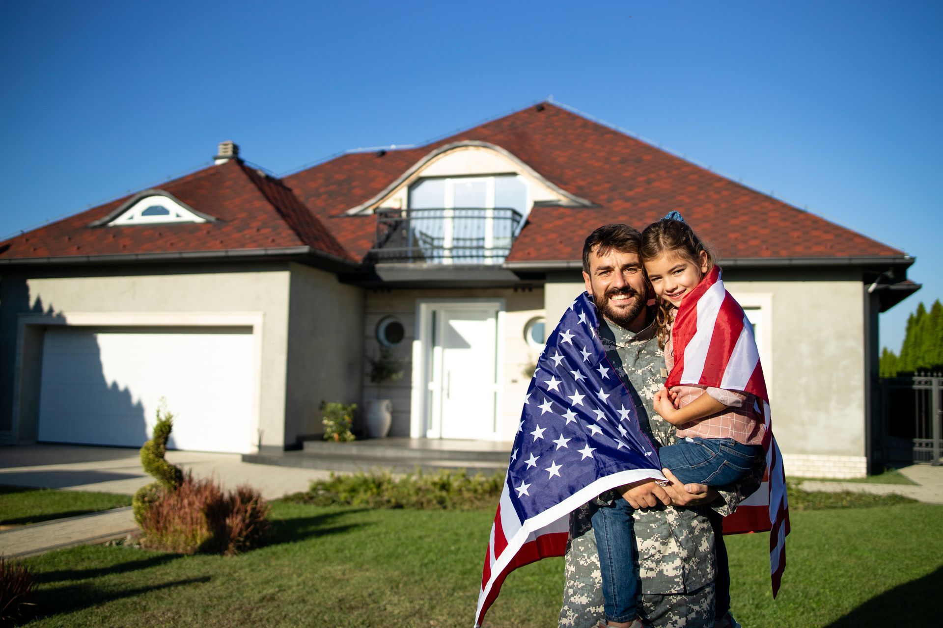 Smiling couple wrapped in an American flag standing in front of a suburban house