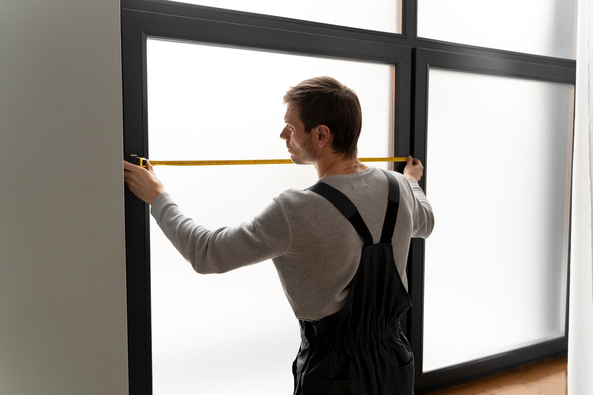 Person measuring a large window with a yellow tape measure in a bright room
