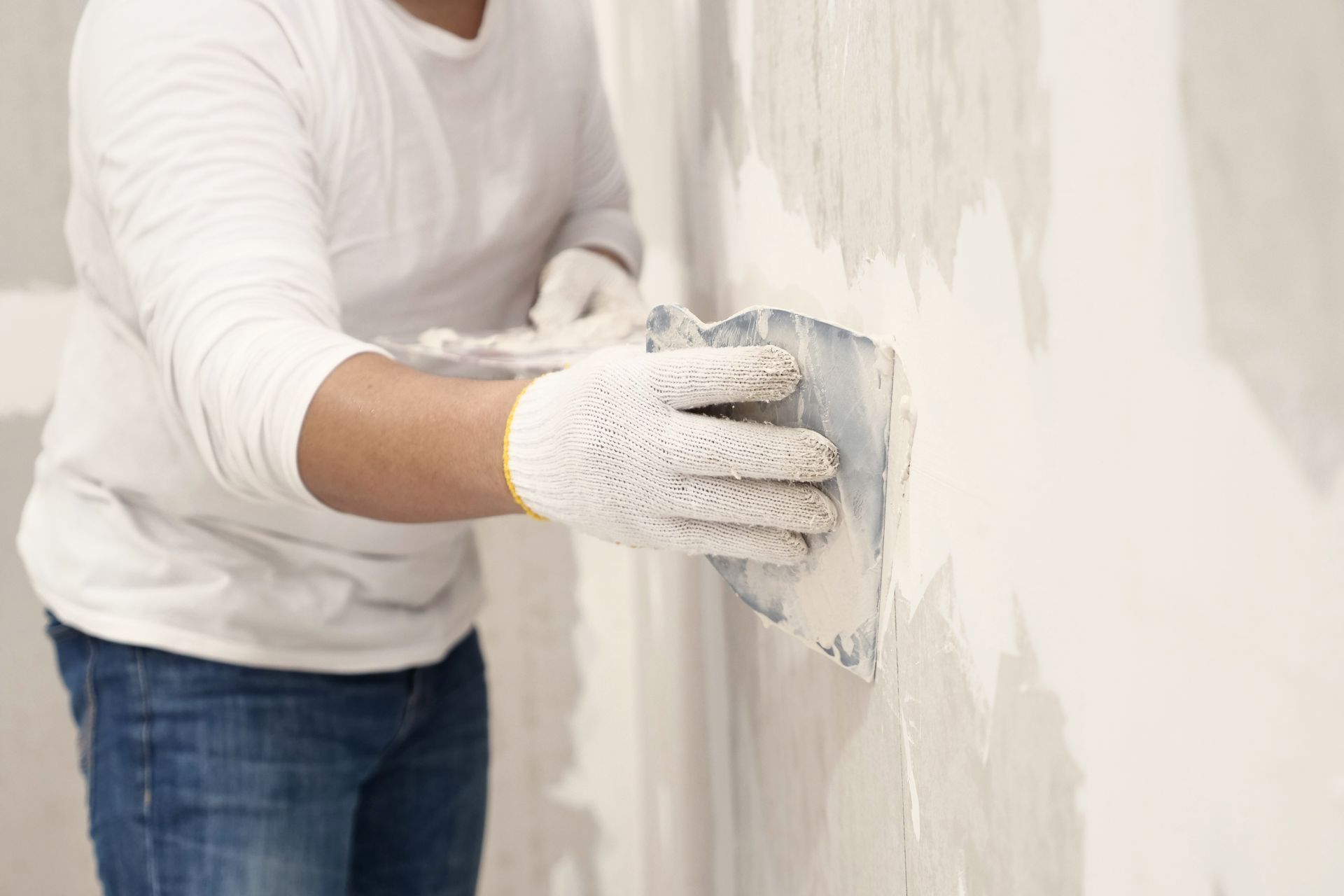 Person smoothing plaster on a wall with a trowel while wearing gloves and jeans