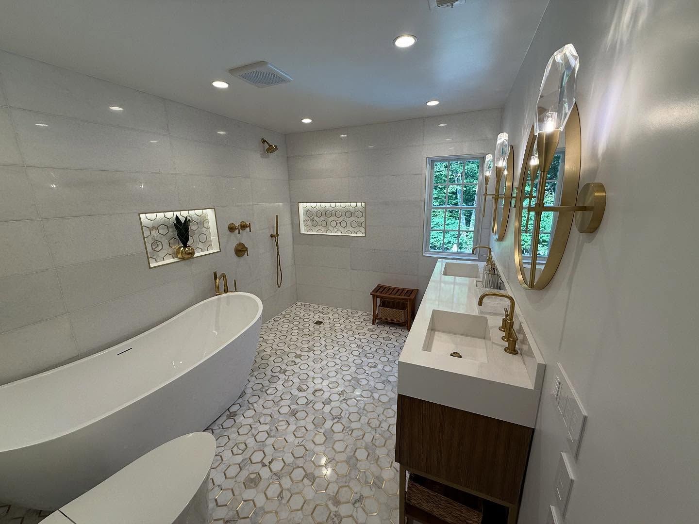 Modern bathroom with white walls, patterned floor, soaking tub, vanity, and gold fixtures.