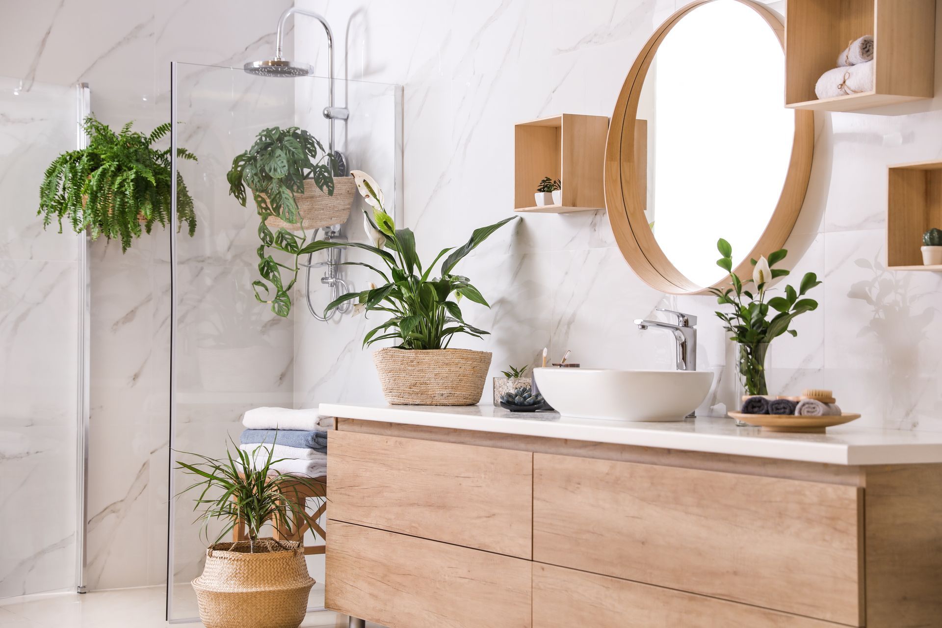 Bright bathroom with wood vanity, round mirror, white sink, and hanging green plants