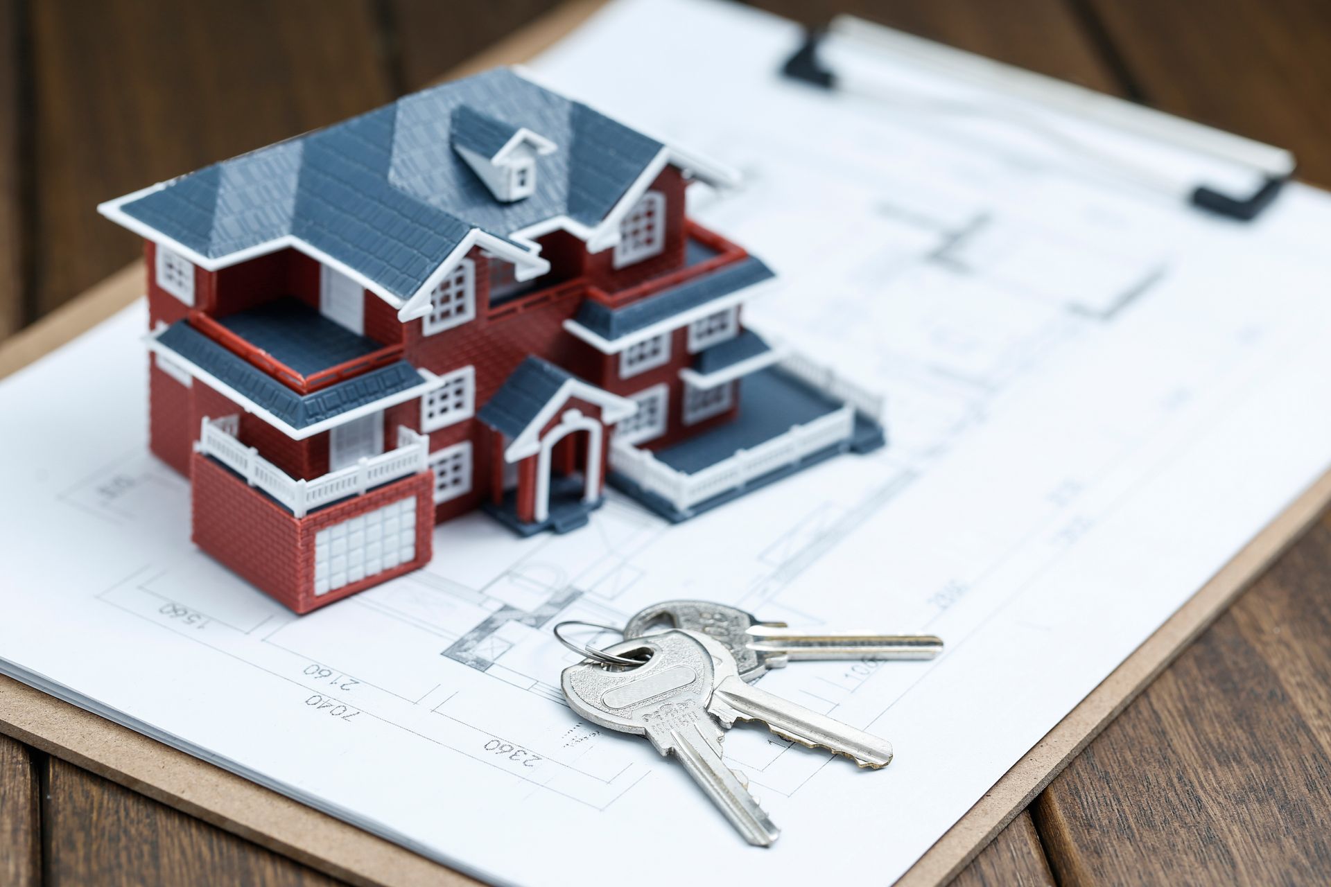 Miniature house model with keys on blueprints, suggesting real estate or home buying