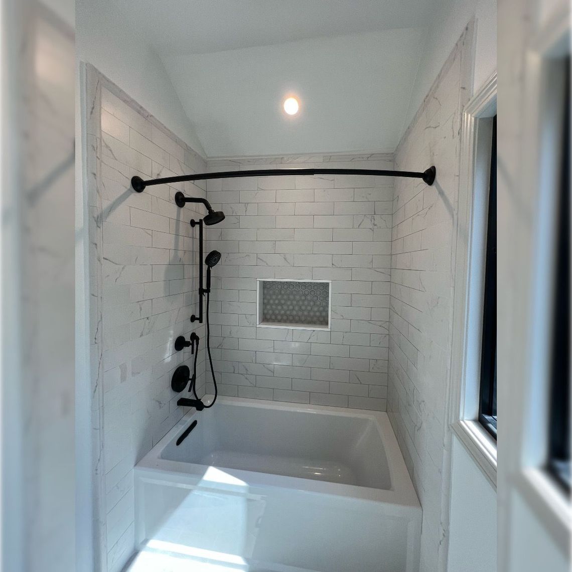 Small white tiled bathroom with a tub, black shower fixtures, and a black shower rod.