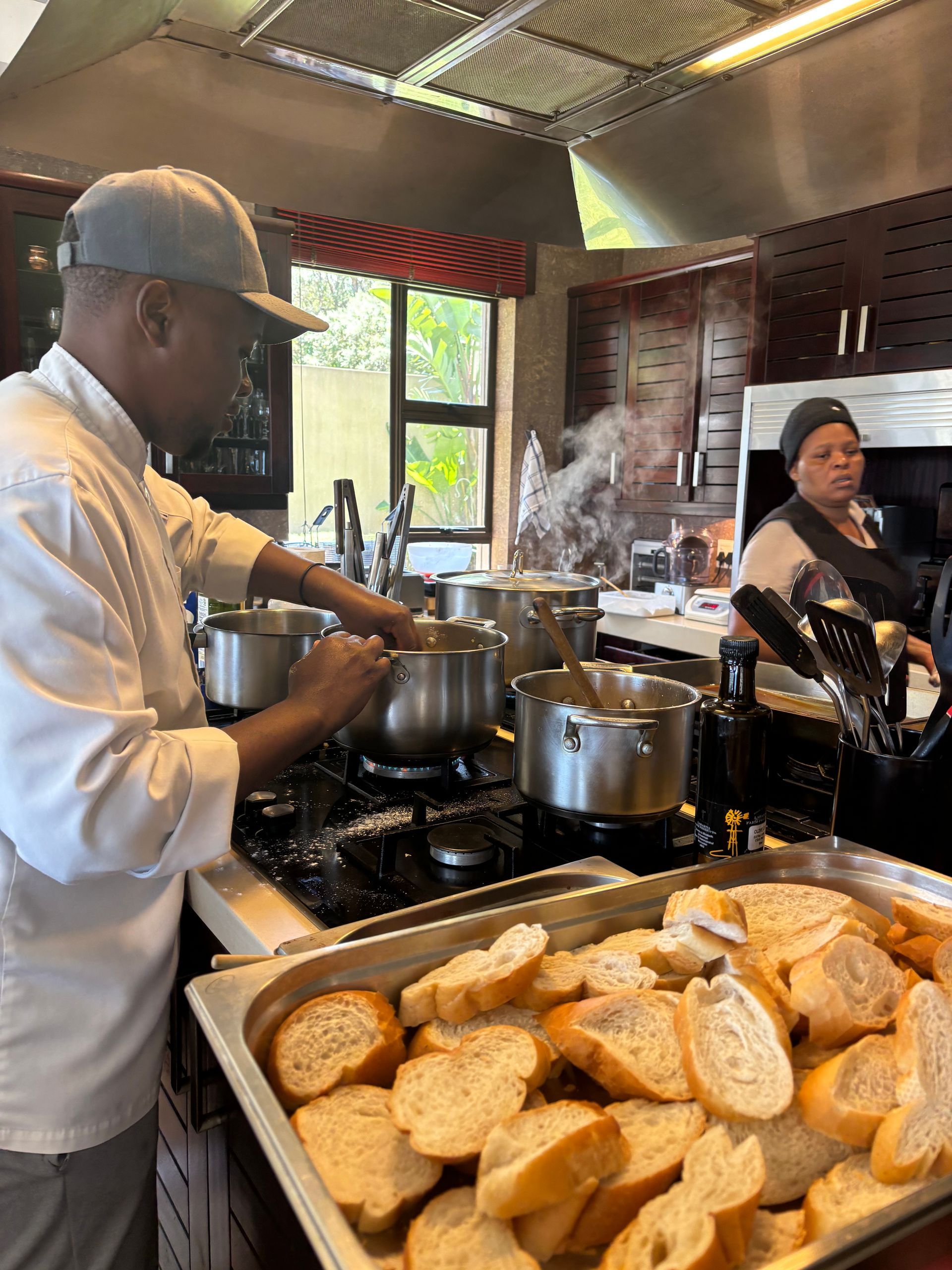 Two chefs cook at a stovetop in a kitchen, with a tray of sliced bread in the foreground.