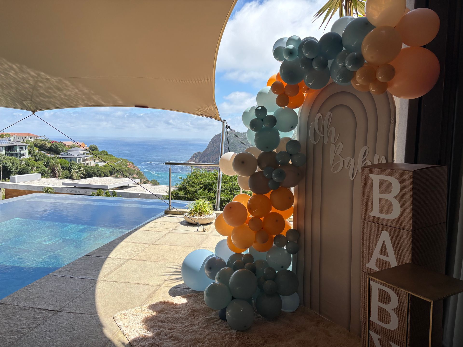 A baby shower decoration with a blue and tan balloon arch next to a