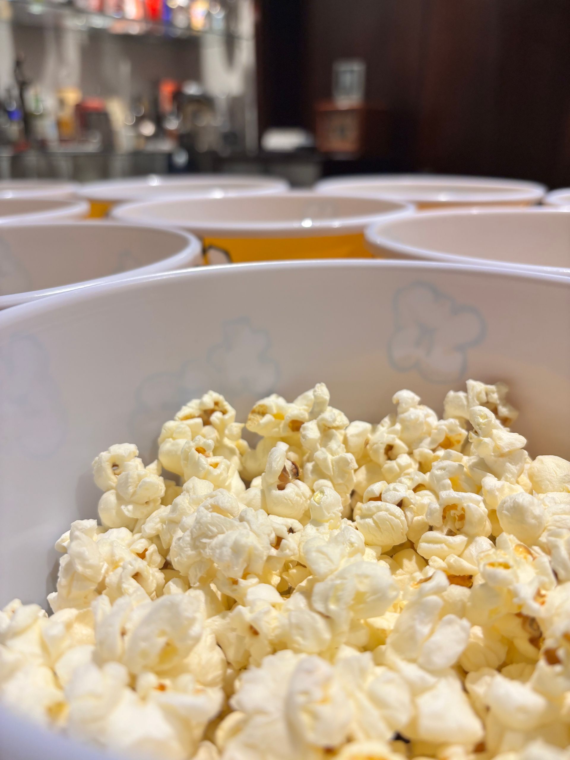 Close-up of a white bowl filled with popcorn, with other bowls blurred in the background.