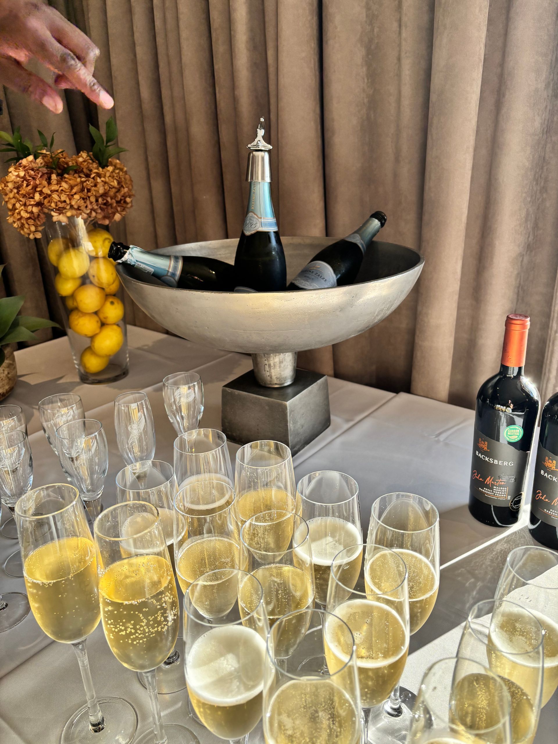 A table set with champagne flutes, a large bowl filled with wine bottles on ice, and two red wine bottles.