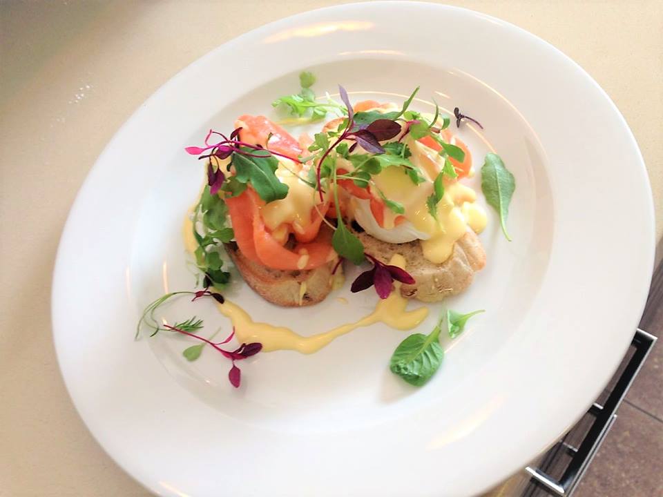 Eggs Benedict with smoked salmon, hollandaise sauce, and microgreens on a white plate.