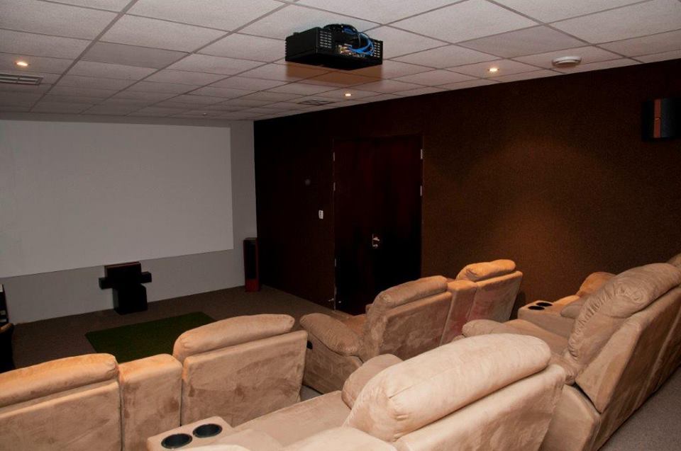 Home theater with reclining chairs, screen, projector, and dark brown wall.
