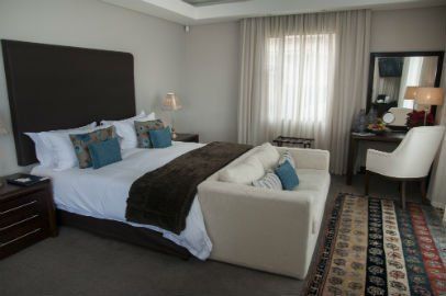 Bedroom with a large bed, sofa, vanity, window with sheer curtains, and area rug.