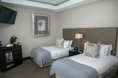 Hotel room with two twin beds, bedside table, TV, and mini-fridge.