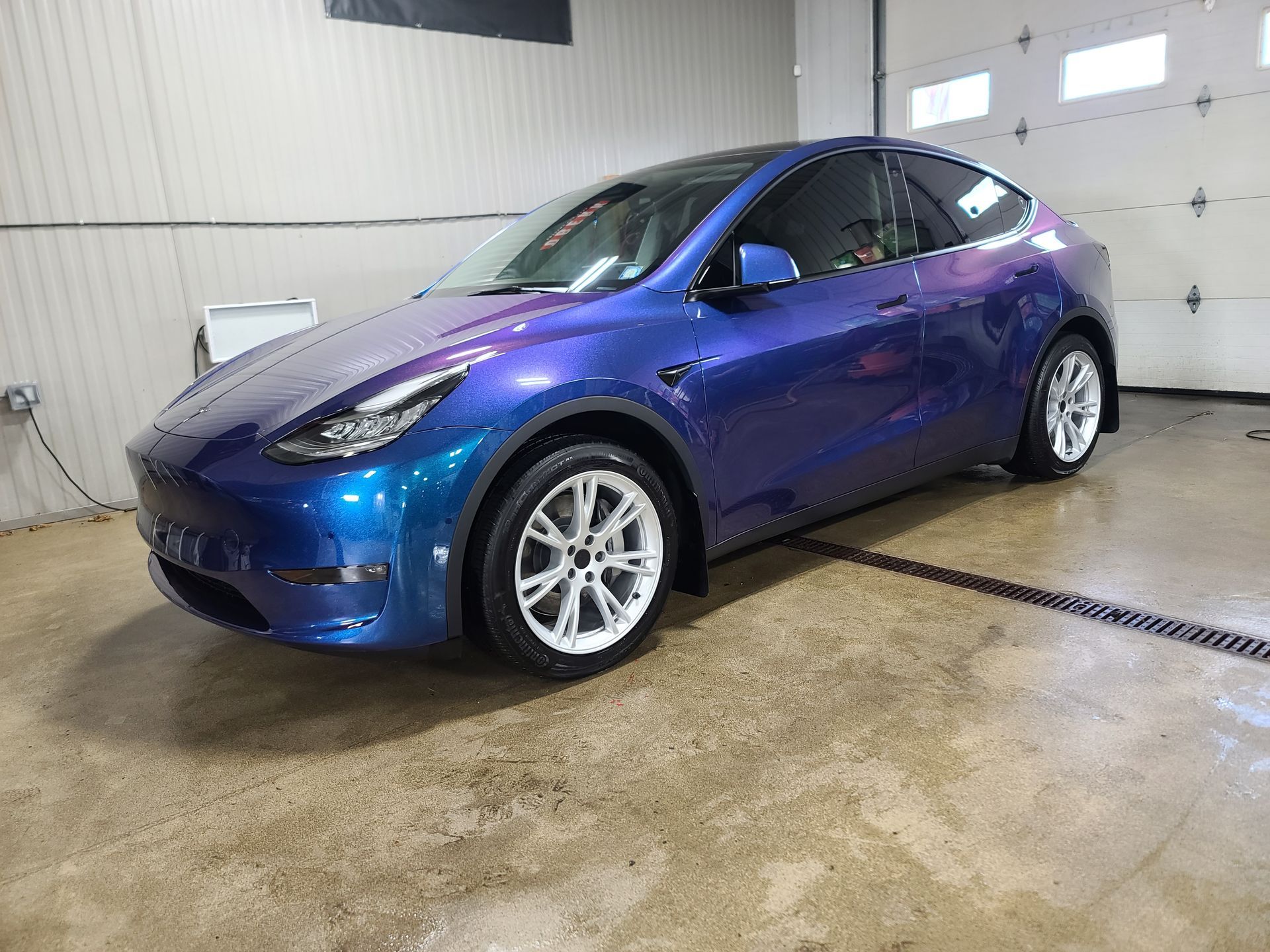Blue compact car parked indoors in a garage, viewed from the front-left side.
