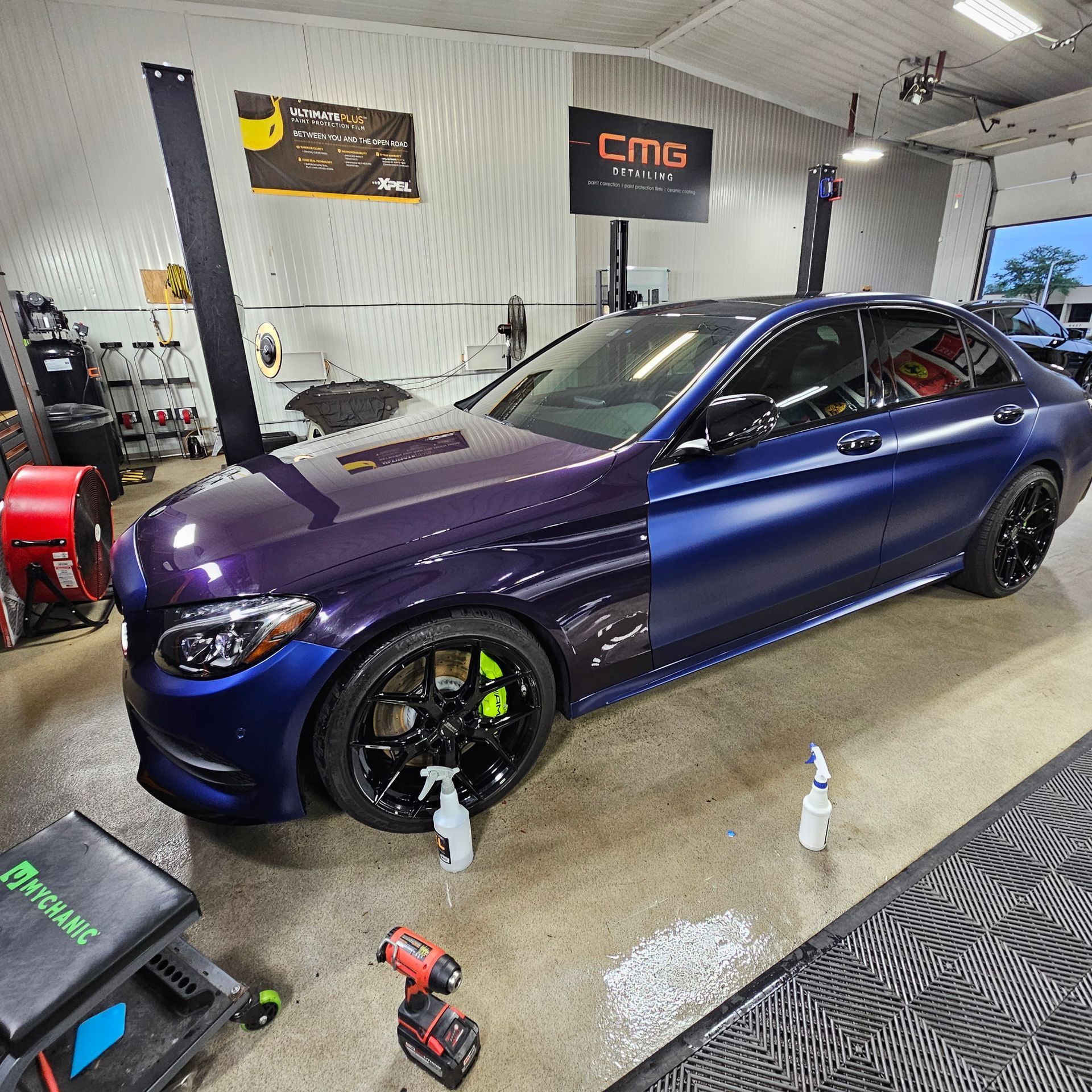A two-tone blue and purple car in a garage with black rims and green brake calipers.