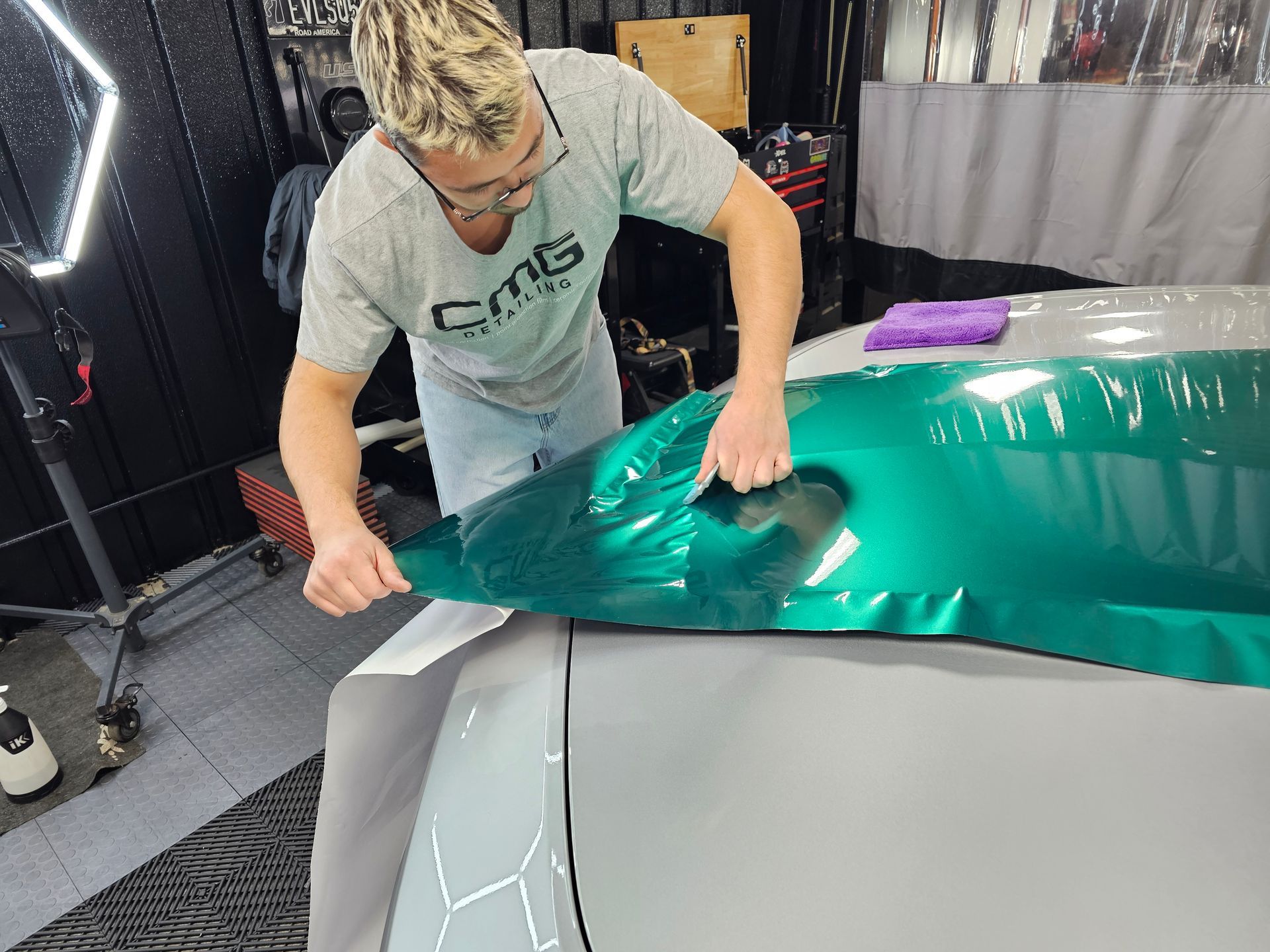 Person applying green vinyl wrap to a car in a workshop