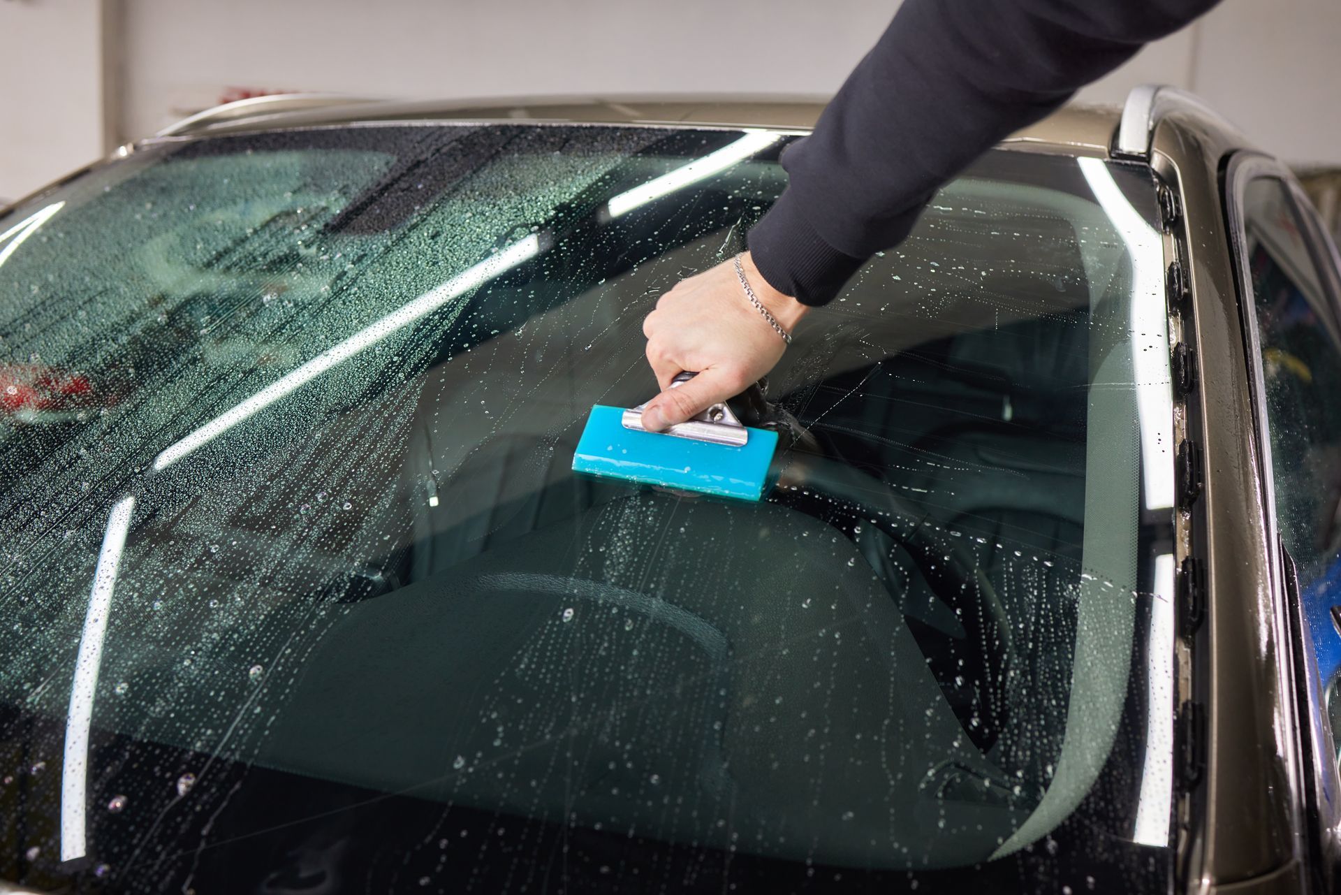 Person squeegeeing soapy water from a car windshield.