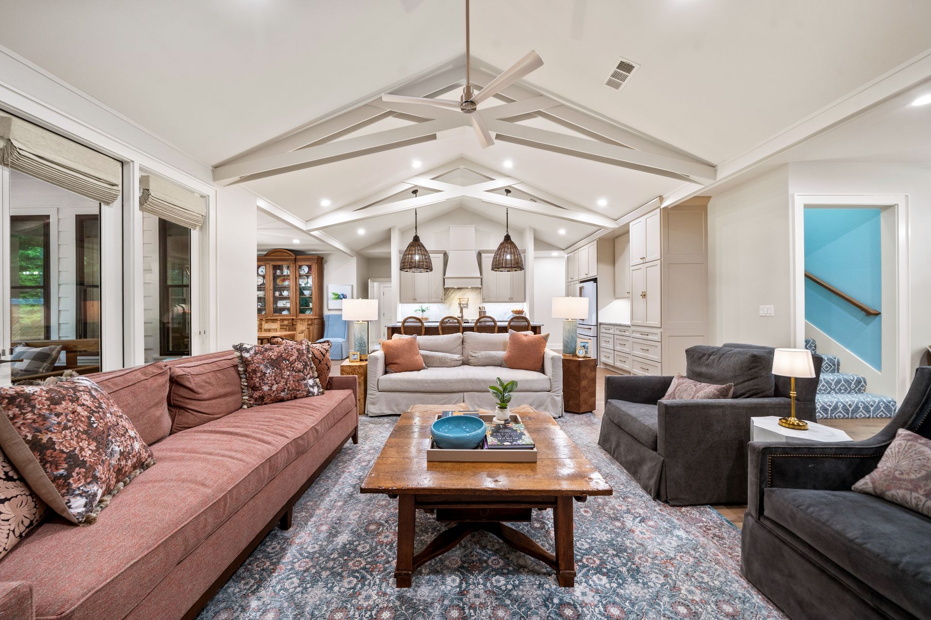 A spacious living room with a vaulted ceiling, a large pink sofa, a wooden coffee table, and dark gray armchairs.