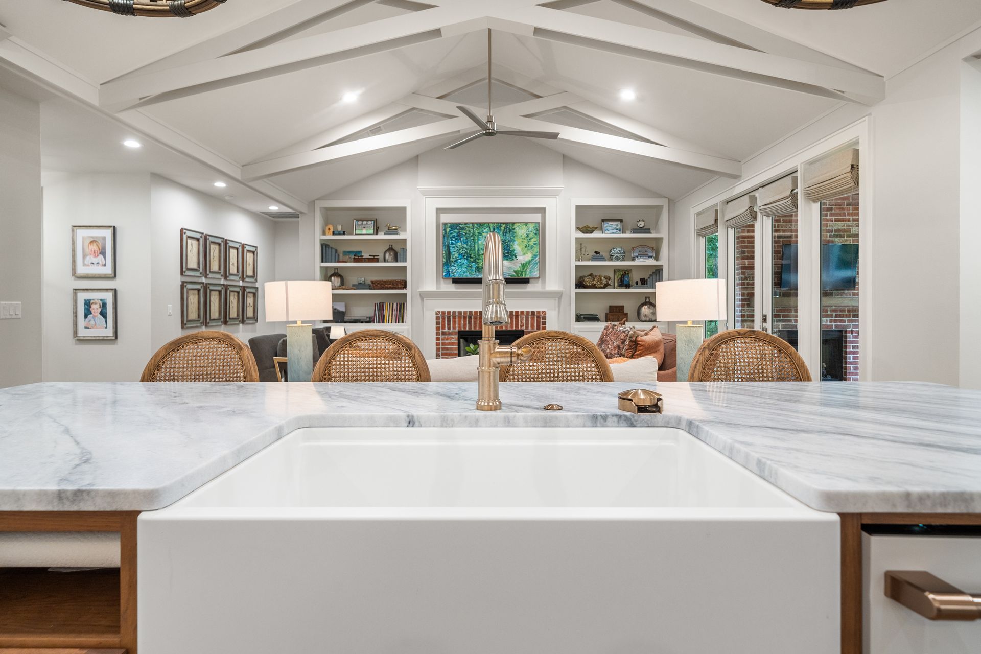 A white farmhouse-style kitchen sink centers a marble island, overlooking a living room with a fireplace and built-ins.
