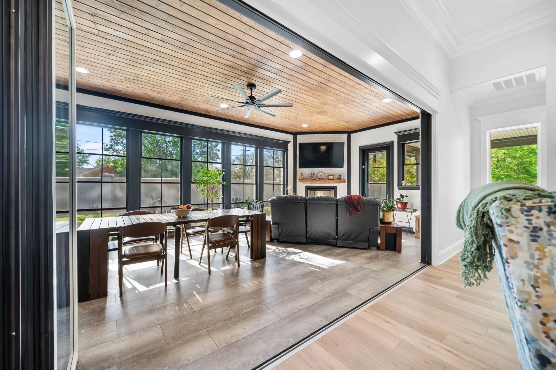 A light-filled sunroom with a wood-slatted ceiling, dining table, and seating area, visible through large open doors.