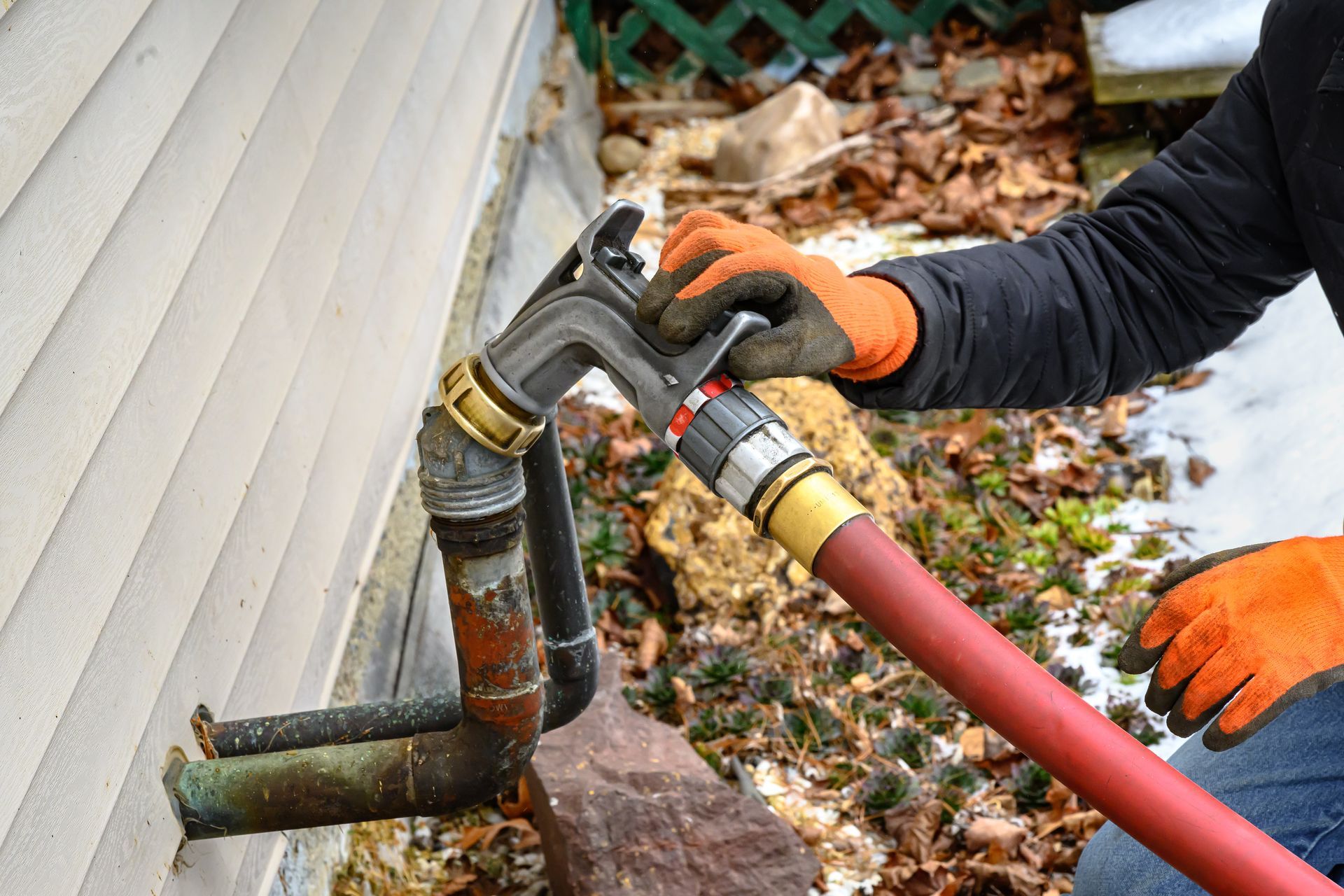 Delivery worker in orange gloves connecting a red fuel hose to a residential heating oil fill pipe Delivery worker in orange gloves connecting a red fuel hose to a residential heating oil fill pipe