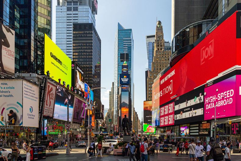 Busy Times Square street with bright billboards, tall buildings, and crowds of pedestrians at dusk