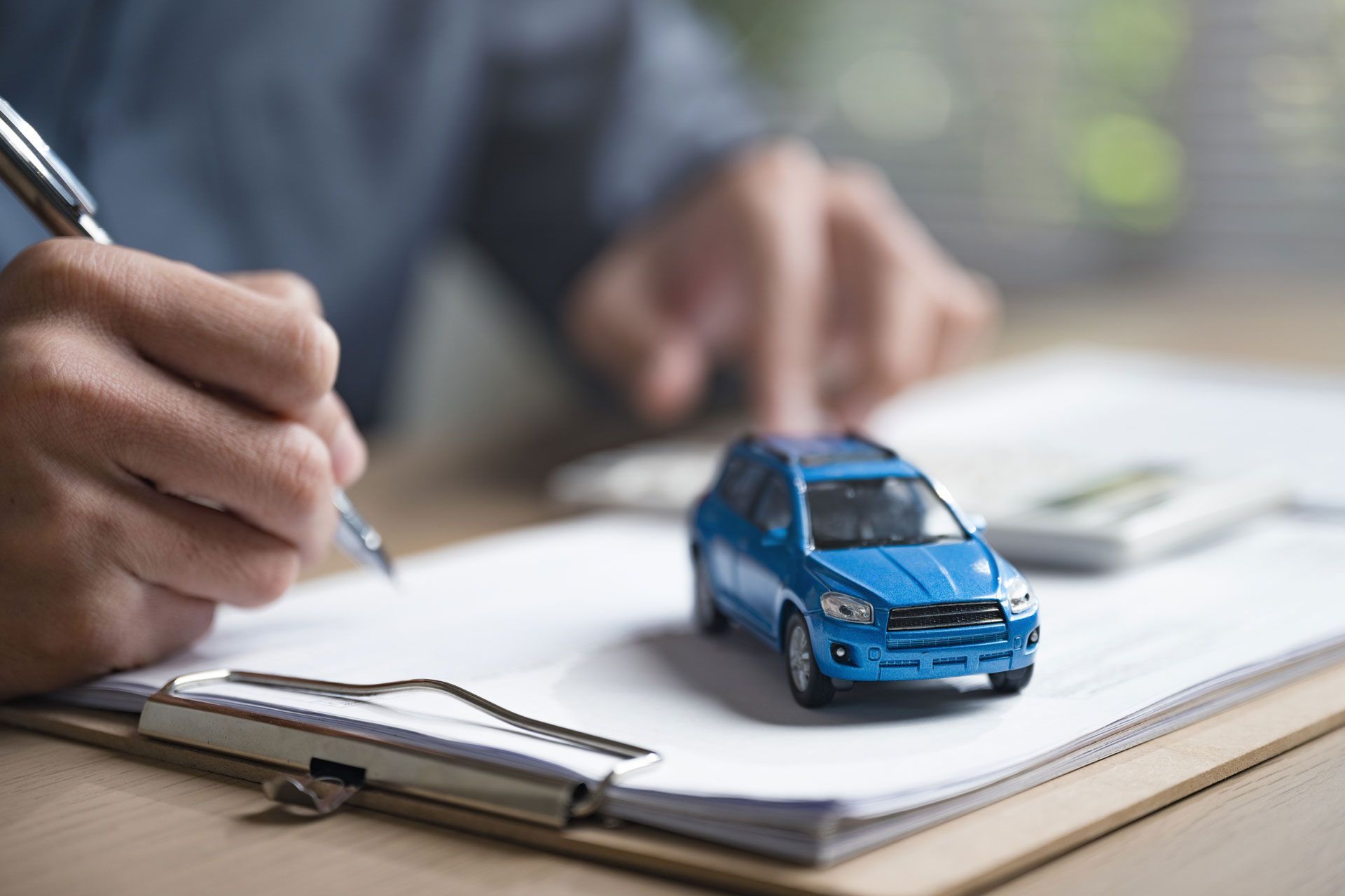 Person writing on paper, blue toy car on clipboard.