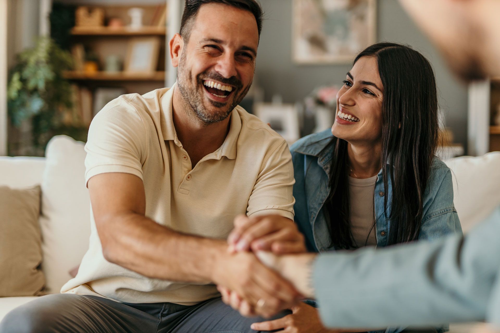 Couple shaking hands with a person, smiling in a home setting.