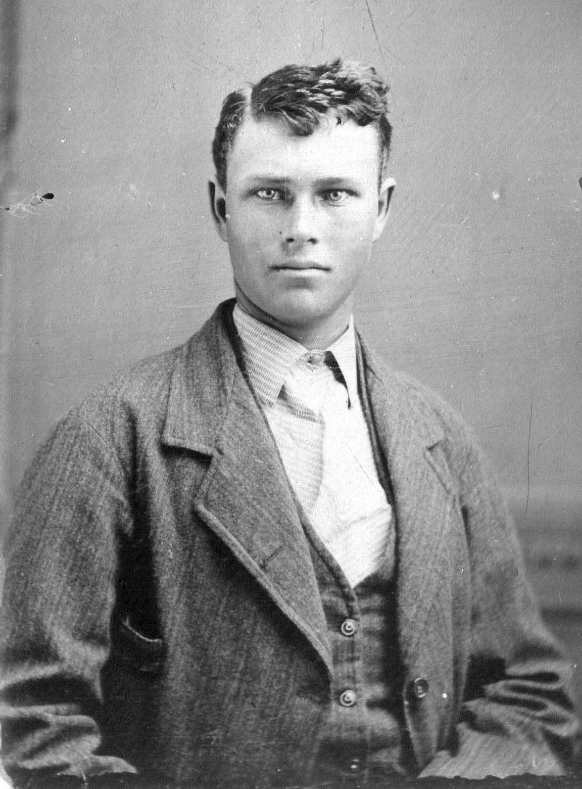 Black-and-white portrait of a young man in a suit jacket, facing forward with a neutral expression.