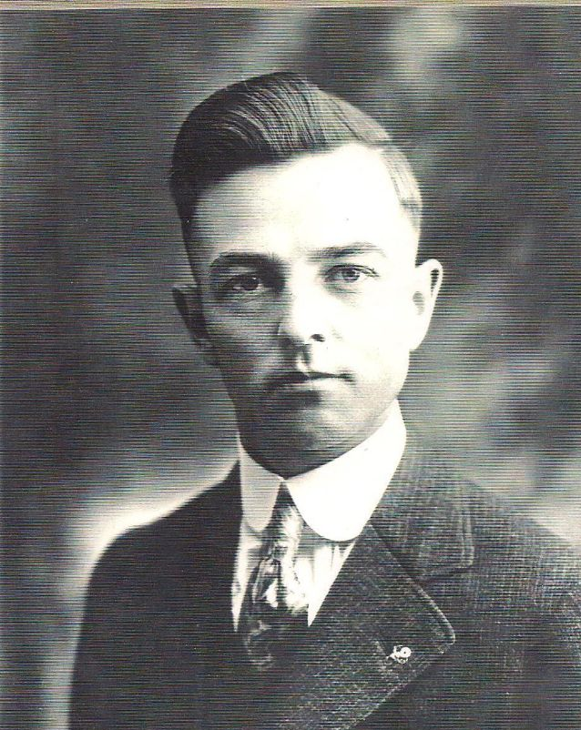 Black-and-white formal portrait of a man in a suit and tie, facing the camera with a neutral expression.